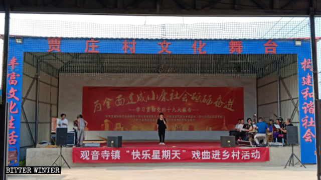 贾庄村文化戏台正在演出，戏台上挂着“快乐星期天”的横幅